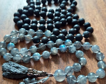 May include: Three strands of beaded necklaces. The top strand features black, porous beads. The middle strand has a mix of black and gray beads. The bottom strand is made of clear, iridescent beads with a gray tassel.
