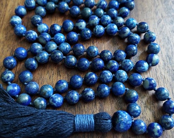 May include: A blue lapis lazuli mala with a dark blue tassel. The mala is made of round beads and is strung on a dark blue cord.