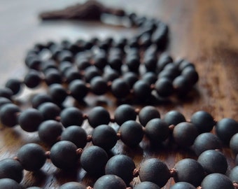 May include: A dark brown wooden mala bead necklace with a tassel. The beads are round and smooth, and the necklace is strung with a brown cord.