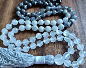 Può includere: Un mala di pietra di luna bianca con un fiocco grigio. Il mala è fatto di perline rotonde ed è infilato su un cordoncino bianco. Il fiocco è fatto di un tessuto morbido e grigio.