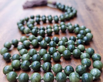 Puede incluir: Un collar de cuentas mala de jade verde con un borla. Las cuentas son redondas y tienen un patrón de mármol.