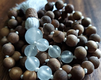 May include: A mala or prayer beads made of dark brown wood with white beads interspersed throughout. The mala has a white tassel.