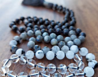 May include: A mala or prayer beads made with clear quartz, labradorite, and black obsidian stones. The beads are strung on a black cord and have a black tassel.