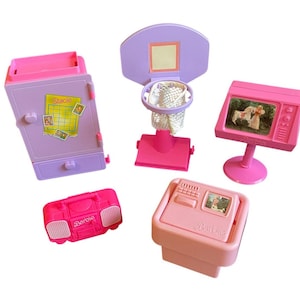 May include: A set of pink and purple Barbie playset furniture, including a refrigerator with a drawer, a basketball hoop with a net, a television with a screen, a boombox, and a small table with a drawer. The refrigerator has a sticker that says "Stacie" on it. The television has a screen that shows a cartoon image of Barbie and a friend. The boombox has the word "Barbie" printed on it.