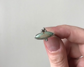 May include: A silver ring with a green and white oval-shaped stone set in the center. The ring has three small silver balls on the top.