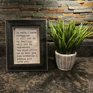 May include: A framed print with a black frame and a white background. The print features a text excerpt from a book. The text reads: "In vain I have struggled, It will not do. My feelings will not be repressed. You must allow me to tell you how ardently I admire and love you."