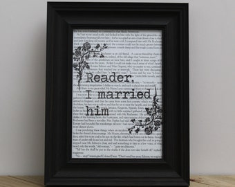 May include: Black framed print with text from a book page. The words "Reader, I married him" are prominently displayed in a bold, vintage font, with floral accents. The print is set on a wooden surface.