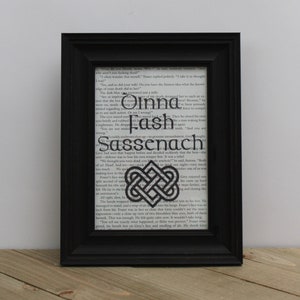 May include: A black framed print with a white background featuring a black and white illustration of a Celtic knot. The text "Oinna Fash Sassenach" is printed in black on the white background.