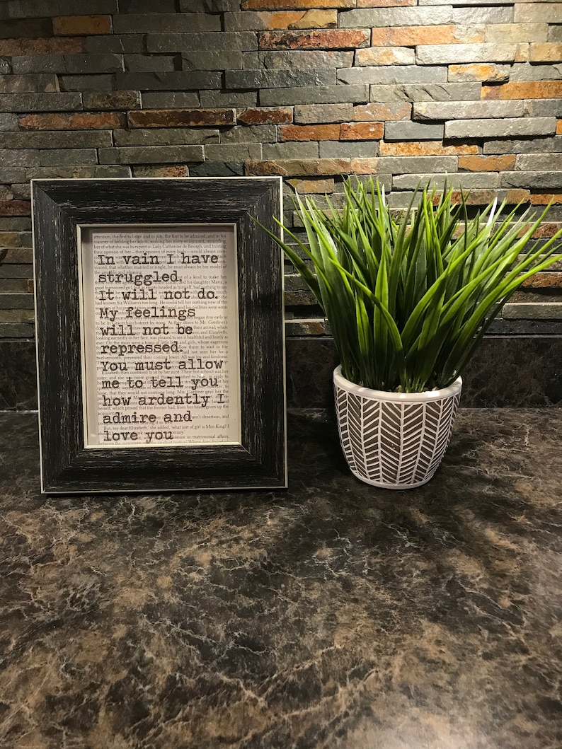 May include: A framed print with a black frame and a white background. The print features a text excerpt from a book. The text reads: "In vain I have struggled, It will not do. My feelings will not be repressed. You must allow me to tell you how ardently I admire and love you."