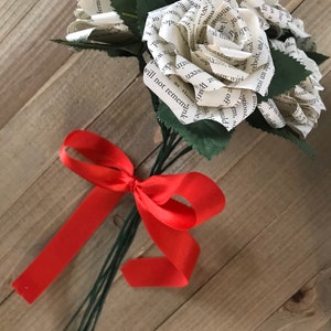 May include: A bouquet of paper roses made from book pages, with green leaves and stems. The bouquet is tied with a bright red ribbon, creating a unique and literary floral arrangement.