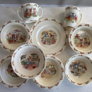 以下が含まれることがあります： ウサギのイラストが描かれたヴィンテージセラミック食器のコレクション。セットには、お皿、ボウル、取っ手付きマグカップが含まれます。お皿とボウルの縁には、繰り返しのウサギ模様が施されています。