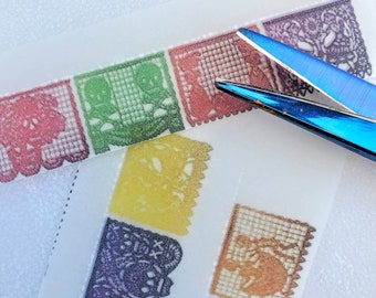 Può includere: Strisce di banner di papel picado colorate con intricati disegni ritagliati, tra cui teschi e motivi floreali. Lo striscione è in vari colori, tra cui rosso, verde, giallo e viola. Un paio di forbici blu si trova nell'angolo in alto a destra.