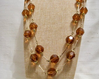 May include: A gold chain necklace with amber-colored faceted glass beads. The necklace is layered with two strands of beads.