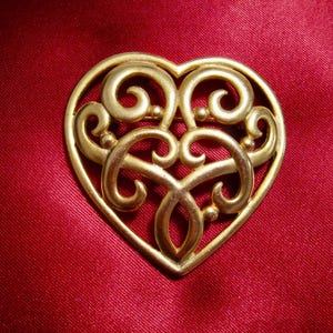 May include: A gold-toned heart-shaped brooch with an intricate, filigree design.