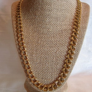 Peut inclure: Un collier en chaîne dorée sur un mannequin recouvert de tissu. La chaîne est composée d'anneaux entrelacés.