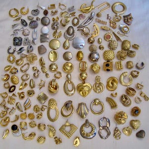Könnte beinhalten: Eine Sammlung von Vintage-Ohrringen in verschiedenen Stilen und Designs, darunter Clip-On- und Stecker-Ohrringe. Die Ohrringe sind überwiegend goldfarben, mit einigen silbernen und gemischten Metallakzenten. Stile umfassen Creolen, Ohrstecker, Anhänger und Statement-Stücke.