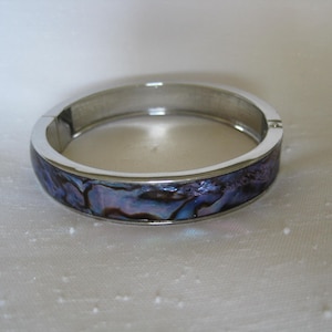 May include: A silver bangle bracelet with a blue, purple, and iridescent abalone shell inlay.
