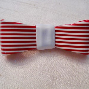 May include: A red and white striped bow tie with a white centre. The bow tie is made of plastic and has a glossy finish.