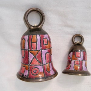 May include: Two ceramic bells with a geometric pattern in shades of pink, orange, and brown. The bells have a loop at the top for hanging.