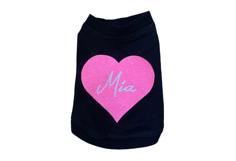 Puede incluir: Camiseta negra para perro con un coraz&oacute;n rosa de purpurina que dice "Mia" en &eacute;l.
