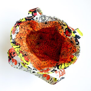 Pu&ograve; includere: Una borsa in tessuto con una stampa a tema Halloween raffigurante scheletri, zucche e pipistrelli su sfondo bianco. L'interno &egrave; foderato con un tessuto arancione brillante decorato con un motivo a ragnatela nera e due manici robusti.