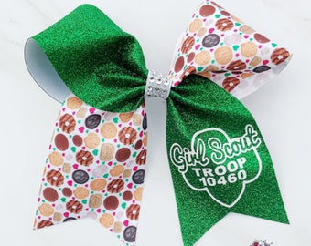 May include: A large green glitter hair bow with a silver rhinestone center. The bow features a pattern of Girl Scout cookies on white fabric and the text "Girl Scout Troop 10460" in white.