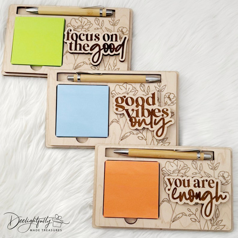 May include: Three wooden memo pad holders with pens, each featuring a different inspirational quote: "focus on the good," "good vibes only," and "you are enough." Each holder includes a notepad and a bamboo pen.