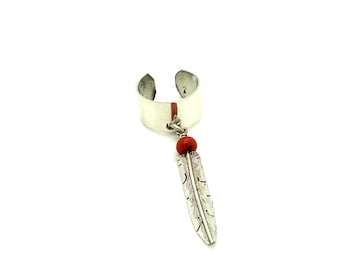 May include: Silver-tone ear cuff with a dangling feather pendant. The cuff features a red bead and a detailed feather charm. The jewelry is set against a white background.