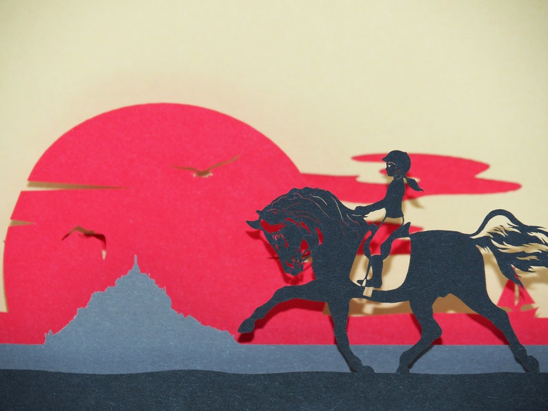 May include: A black silhouette of a person riding a horse against a red sunset background. The horse is rearing up on its hind legs. The person is wearing a helmet and riding in a riding position. The background is a red sunset with a gray mountain in the foreground.