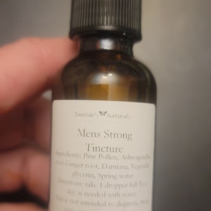 May include: A brown glass bottle with a dropper top and a white label that reads "Jamilah's Naturals Mens Strong Tincture". The label lists the ingredients: Pine Pollen, Ashwagandha root, Ginger root, Damiana, Vegetable glycerin, Spring water. The label also includes directions for use: take 1 dropper full 3 times a day as needed with water. This is not intended to diagnose, treat, cure or prevent any disease.