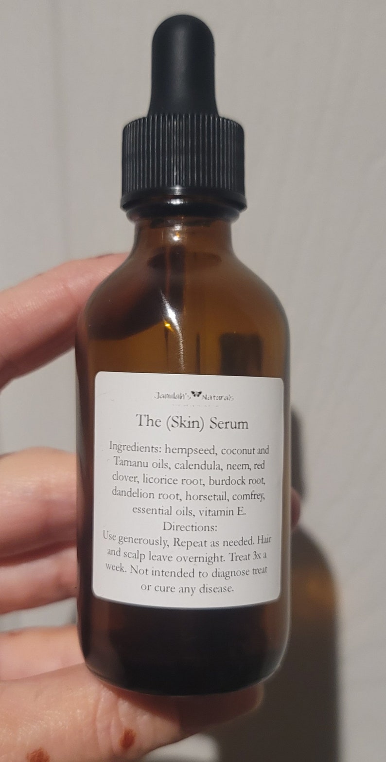Puede incluir: Una botella de vidrio marr&oacute;n con un gotero negro. La etiqueta dice "Jamilah's Naturals The (Skin) Serum" y enumera los ingredientes, que incluyen semillas de c&aacute;&ntilde;amo, coco, aceites de tamanu, cal&eacute;ndula, neem, tr&eacute;bol rojo, ra&iacute;z de regaliz, ra&iacute;z de bardana, ra&iacute;z de diente de le&oacute;n, cola de caballo, consuelda, aceites esenciales y vitamina E. Tambi&eacute;n se incluyen las instrucciones de uso.