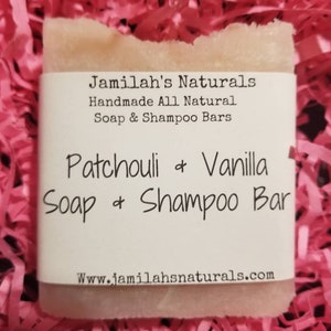 May include: A bar of handmade soap and shampoo in a light pink color with a white label that reads "Jamilah's Naturals Handmade All Natural Soap & Shampoo Bars Patchouli & Vanilla Soap & Shampoo Bar Www.jamilahsnaturals.com"