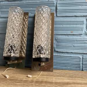 Puede incluir: Un par de apliques de pared plateadas con pantallas de vidrio transparente con un patrón de diamante. Las apliques tienen acentos negros y están montadas en una pared de ladrillo.
