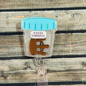 May include: A clear, glitter-filled badge reel with a light blue lid and the words "STOOL SAMPLE." The badge features a brown stool graphic. The reel has a silver clip and a clear plastic strap.