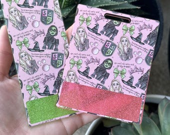May include: Two pink badge holders with a repeating pattern of illustrations, including a witch hat, a bow, and a shield. One has a green glitter bottom, the other a red glitter bottom. Text includes "we can't all come and go by bubble."
