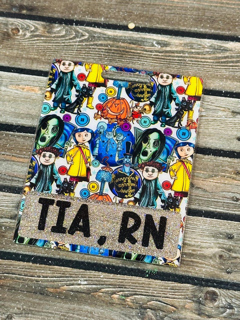 Peut inclure: Un porte-badge rectangulaire avec une bordure scintillante et le texte "TIA. RN". Le badge pr&eacute;sente un motif color&eacute; de personnages de dessins anim&eacute;s et de boutons. Le fond est une surface en bois.