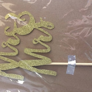 Puede incluir: Topper para pastel de brillo dorado con las palabras "Mr & Mrs" en un palo de madera.