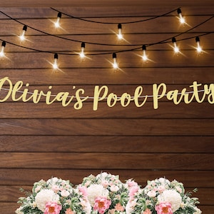 May include: Gold glitter banner with the text "Olivia's Pool Party" hanging on a wood background with string lights.