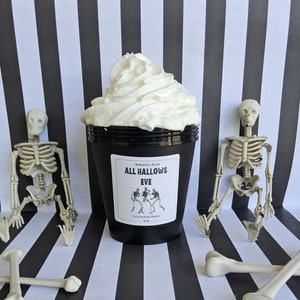 K&ouml;nnte beinhalten: Ein schwarzer Beh&auml;lter mit einem wei&szlig;en Etikett, auf dem "Butterfly Kisses All Hallows Eve Whipped Body Butter 8 oz" steht, ist von zwei wei&szlig;en Skeletten aus Plastik und zwei wei&szlig;en Knochen aus Plastik umgeben. Der Beh&auml;lter ist mit wei&szlig;er, geschlagenem K&ouml;rperbutter gef&uuml;llt.