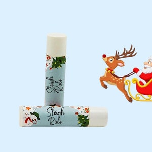 May include: Two white lip balm tubes with a Christmas theme. The tubes have a blue background with a green Christmas tree, a snowman, and the text "Sleigh Ride".
