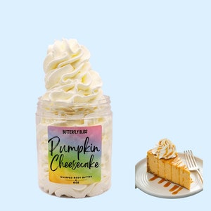 May include: A jar of whipped body butter with a label that reads "Butterfly Bliss Pumpkin Cheesecake Whipped Body Butter 8 oz". The jar is filled with a white whipped cream-like substance. A slice of pumpkin cheesecake is shown in the background.