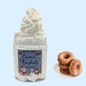May include: A white whipped body butter in a clear jar with a festive label that reads "Butterfly Bliss Cinnamon Doughnuts Whipped Body Butter". The label features a snowman, Santa Claus, and a Christmas tree.  There are four cinnamon sugar donuts on a white plate.