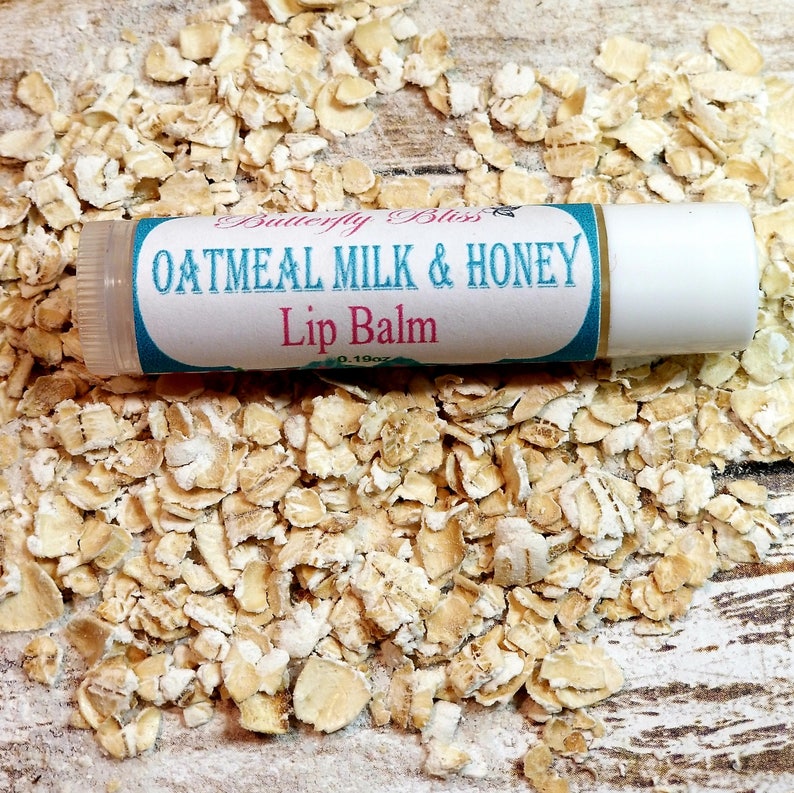 May include: A white lip balm tube with a blue and pink label that reads "Butterfly Bliss Oatmeal Milk & Honey Lip Balm 0.19oz". The tube is sitting on a bed of rolled oats.