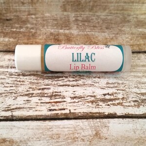 May include: A white tube of lip balm with a teal and gold label that reads "Butterfly Bliss Lilac Lip Balm".