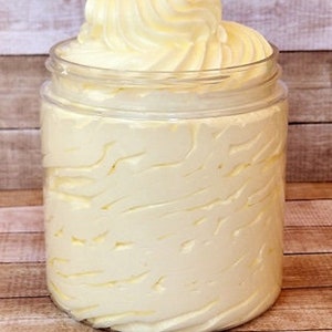 May include: A clear glass jar filled with a thick, white whipped body butter. The butter is swirled and has a smooth, creamy texture.