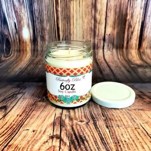 K&ouml;nnte beinhalten: Eine 6 oz Sojawachskerze in einem durchsichtigen Glasgef&auml;&szlig; mit einem bunten Etikett, auf dem "Butterfly Bliss 6 oz Soy Candle" steht.
