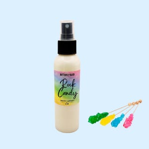 Puede incluir: Una botella de spray corporal blanca con una tapa negra y una etiqueta colorida que dice "Butterfly Bliss Rock Candy Body Spray 4 oz." Cuatro palitos de caramelo de roca coloridos están al lado de la botella.
