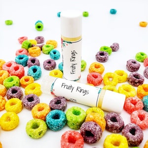 Peut inclure: Deux tubes de baume &agrave; l&egrave;vres blancs avec un motif floral color&eacute; et le texte "Fruity Rings" sur l'&eacute;tiquette. Les baumes &agrave; l&egrave;vres sont entour&eacute;s d'anneaux de c&eacute;r&eacute;ales color&eacute;s.