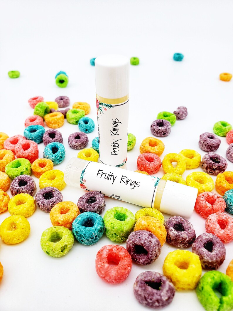 Peut inclure: Deux tubes de baume &agrave; l&egrave;vres blancs avec un motif floral color&eacute; et le texte "Fruity Rings" sur l'&eacute;tiquette. Les baumes &agrave; l&egrave;vres sont entour&eacute;s d'anneaux de c&eacute;r&eacute;ales color&eacute;s.