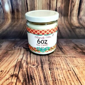 May include: A 6 oz soy candle in a clear glass jar with a white lid. The jar has a red, white, and blue patterned label with the text "Butterfly Bliss 6 oz Soy Candle".
